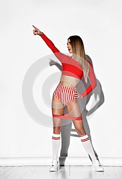 Young sexy woman in red striped sportswear, long socks and sneakers standing with fitness flex on legs and showing up