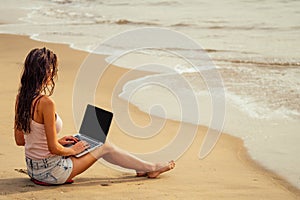 Young sexy woman in stylish glasses using laptop freelancing on the tropical paradise beach. Girl freelancer work