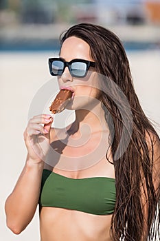 Young sexy woman in sunglasses and bikini eat icecream on the beach