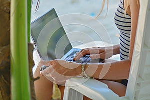 Young sexy woman using laptop on the beach. Girl Freelancer working. Tropical vacation concept.