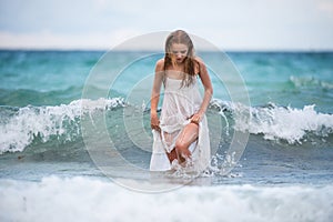 Young sexy woman at waves sea. Summer beach sensual girl. Girl in white dress on tropical beach vacation.