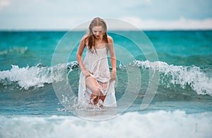 Young sexy woman at waves sea. Summer beach sensual girl. Girl in white dress on tropical beach vacation.