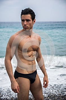 Young shirtless athletic man standing in water by ocean shore