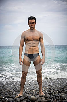 Young shirtless athletic man standing in water by ocean shore