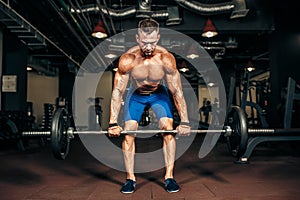 Young shirtless man doing deadlift exercise at gym.