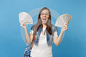 Young shocked amazed woman student in glasses with backpack with closed eyes screaming hold bundle lots of dollars, cash