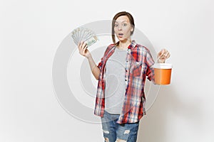 Young shocked beautiful woman in casual clothes holding bundle of dollars, cash money and paint bucket isolated on white