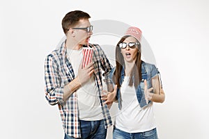 Young shocked couple, woman and man in 3d glasses with bucket for popcorn on head watching movie film on date, holding