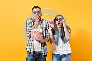 Young shocked couple woman man in 3d glasses watching movie film on date holding bucket of popcorn cup of soda or cola