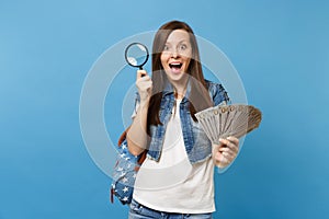 Young shocked excited woman student with backpack holding bundle lots of dollars cash money and magnifying glass