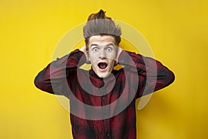 Young shocked guy screaming on a yellow isolated background, hipster with a funny hairstyle is panicking
