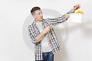 Young shocked handsome man pointing index finger on empty paint bucket with copy space and paint roller for wall