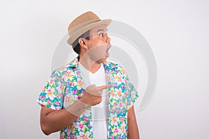 Young shocked man pointing finger into blank space.He`s wearing summer shirt