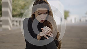 Young shocked woman dressed in black sits on street and looks down