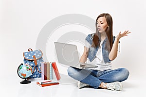 Young shocked woman student holding using laptop pc computer spreading hand sitting near globe backpack, school books