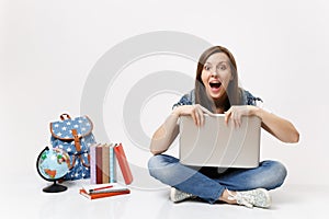 Young shocked woman student with opened mouth holding clinging to laptop pc computer sitting near globe backpack school