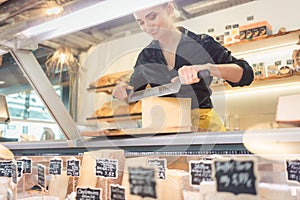 Young shop clerk in deli cutting cheese