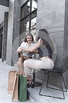 Young shopaholic friends women friends sit in street coffed cafe and talking after shopping and carry shopping