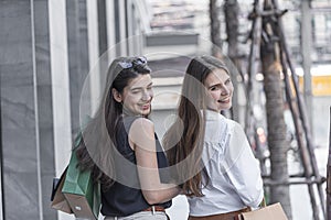 Young shopaholic friends women walking and carry shopping bags in the street city with happy and smiling