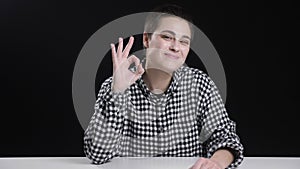 Young short hair girl shows okay sign, smiling, laughing, black background