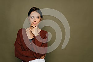 Young short-haired brunette woman. Thinking looking at the left side copy space, supporting her chin with her hand.