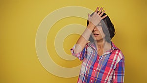 Young short-haired woman with dark hair on yellow background stands. Caucasian model shows sharp recollection. She slaps