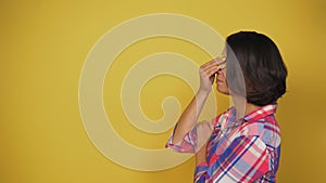 Young short-haired woman with dark hair on yellow background stands in profile. Caucasian model shows sharp recollection