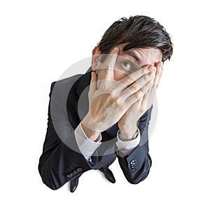 Young shy man is covering his face with hands and looking through fingers. View from above. Isolated on white background