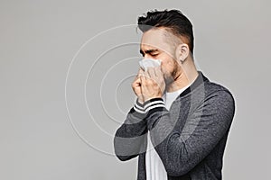 Young sick man having snotty nose, temperature and feeling bad. Sick guy has sneezed,  at grey background with