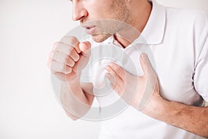 Young sick man isolated over white background. Cut view and close up of guy holding fist close to mouth and cough. Pain