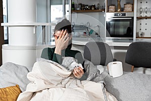 Young sick stressed woman lying at home covered with blanket blowing her nose. Ill female have common cold and flue with runny nos