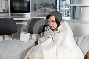Young sick stressed woman lying at home covered with blanket blowing her nose. Ill female have common cold and flue with runny nos