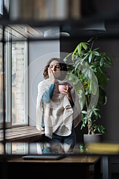 Young sick unhealthy female employee with seasonal flu influenza symptoms drinking hot tea in office