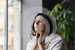 Young sick unhealthy looking woman suffering from sore throat and swollen glands, looking out window