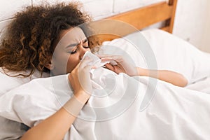 Young sick woman blowing her nose in bed