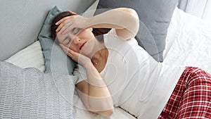 Young sick woman having high temperature lying in bed and holding hand on forehead while suffering from headache