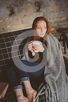 Young sick woman healing with hot drink at home on cozy couch