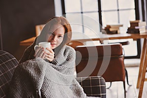 Young sick woman healing with hot drink at home on cozy couch