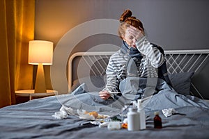 Young sick woman is holding the thermometer, touching her forehead