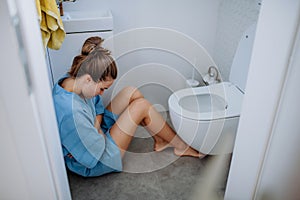 Young sick woman sitting on floor near toilet.