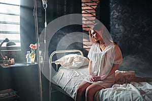 Young sick woman sitting on hospital bed on drip