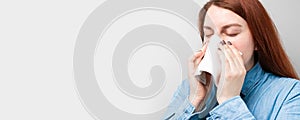 Young sick woman sneezing holding napkin blowout runny nose on a gray background
