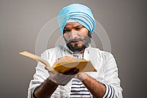 young sikh man reading holy religious Scripture for praying god on grey background - concept of spiritual belifes