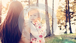 Young single mother holding cute toddler girl daughter in her arms and stroking her hair, girl power concept