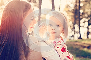 Young single mother holding cute toddler girl daughter in her arms and stroking her hair, girl power concept