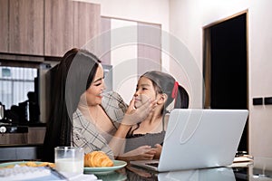 A young single mother receives a snack and eats it with her daughter while she works at home on her laptop.