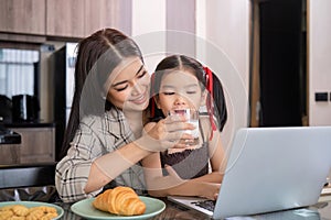 A young single mother receives a snack and eats it with her daughter while she works at home on her laptop.