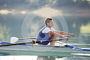 A Young single scull rowing competitor paddles on the tranquil lake