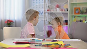 Young sister disturbing elder brother drawing table, family communication, fun