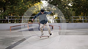 Young skater in casual clothes and black hat sliding from the ramp and making flip trick with board unsuccessfully in